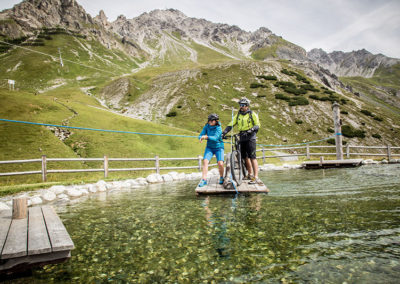 Mountainbiker überqueren See mit Floß