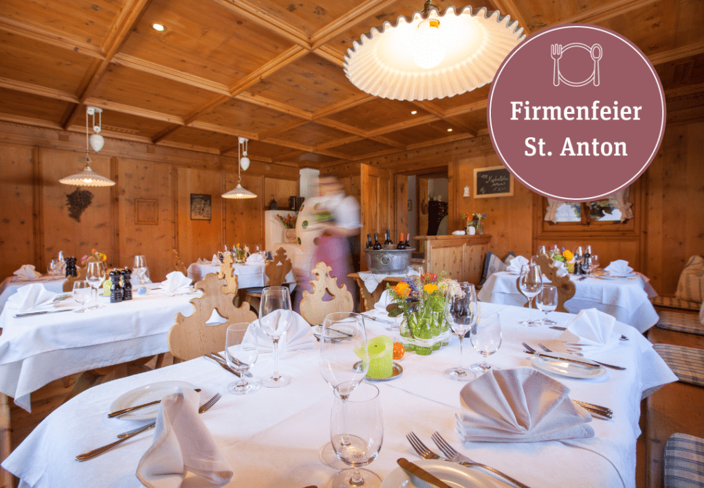 A rustic restaurant interior with wood-paneled walls and set tables, featuring a promotional circular graphic for a company party in St. Anton.