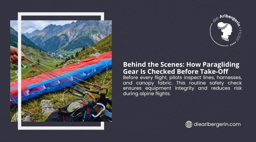 Close-up of a paragliding canopy in red and blue laid out on a grassy mountainside, with lines, carabiners, and harness being inspected, alpine valley in the background.