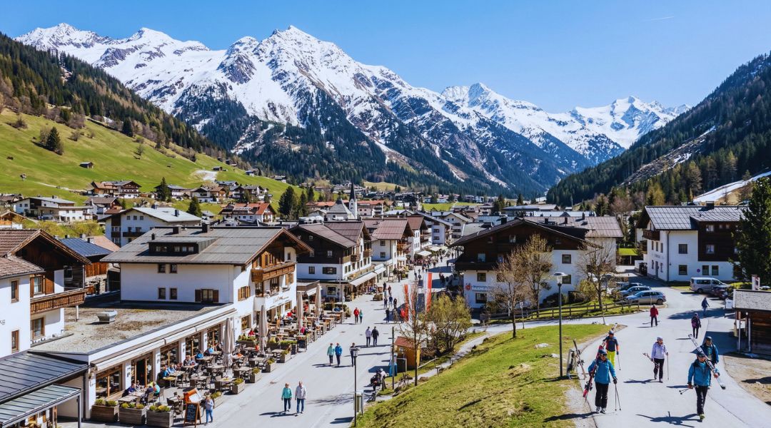 St. Anton am Arlberg village in spring with skiers, outdoor terraces and snow-capped peaks — ideal base for spring activities in 2026.