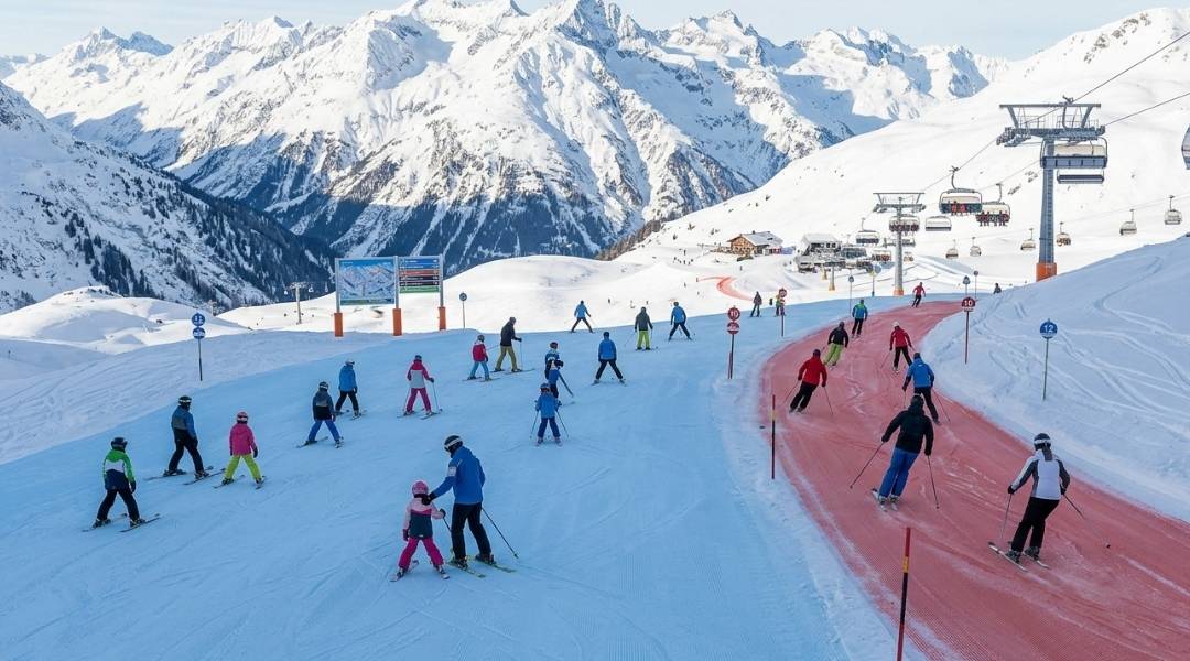 Families and children ski on a wide groomed Arlberg run beside a red carpet lane, illustrating family-friendly ski runs for mixed ability groups.