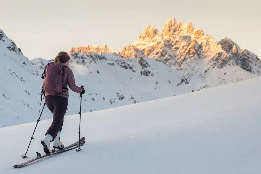 A ski tourer skinning uphill alone at dawn on an empty groomed piste with Arlberg peaks behind