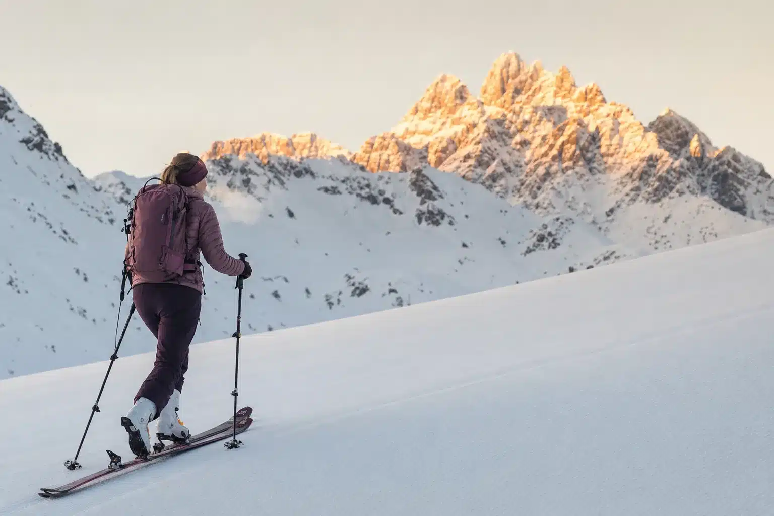 A ski tourer skinning uphill alone at dawn on an empty groomed piste with Arlberg peaks behind
