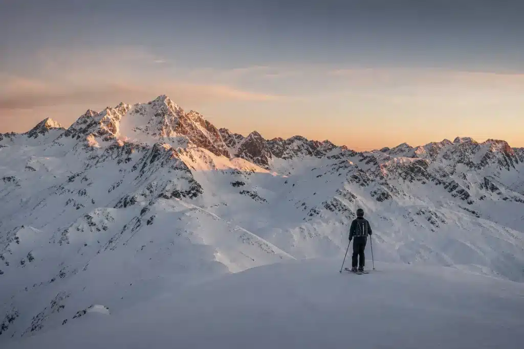 A solo skier at the top of a snow-covered St. Anton piste facing dramatic Alpine peaks in soft dawn light
