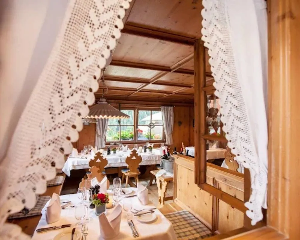 Homepage 14 Traditional wood panelled dining room with white tablecloths and carved chairs, seen through crocheted lace curtains